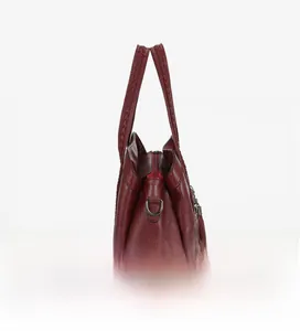 Détail du sac cabas bordeaux avec poignée tressée, pompon en cuir et texture grainée