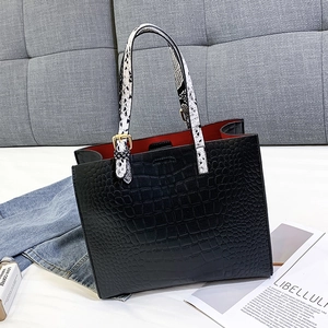 Detail of black faux crocodile tote bag with red lining and snake print top handles