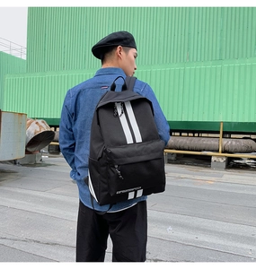 Side view of a black street-style backpack with white stripes on an outdoor model