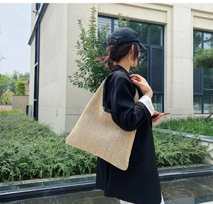Outdoor street shot of large beige woven straw tote bag with black leather shoulder straps