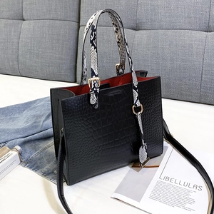 Crocodile texture tote bag with snake pattern handles and red lining on a grey sofa