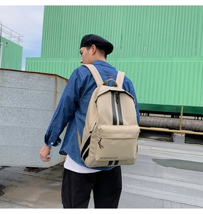 Outdoor shot of a khaki canvas backpack with black racing stripes and zip pockets