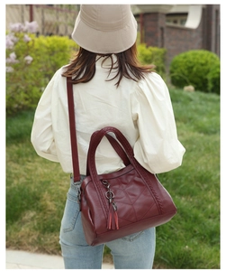 Détail du sac cabas bordeaux avec poignées tressées, coutures en V et pendentif à pompon