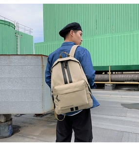 Outdoor view of a khaki casual backpack with black stripes and front zipper pocket