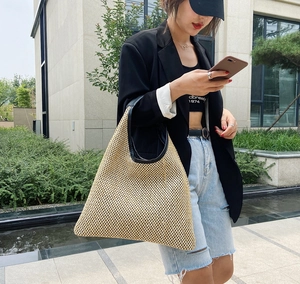 Detail of hand-woven straw beach bag with black leather handles and spacious interior
