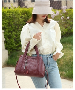 Détail du sac cabas bordeaux avec poignées tressées, texture cuir et pompon décoratif