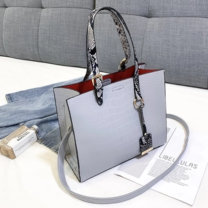 Detail of grey crocodile pattern handbag with snake print handles and red lining texture