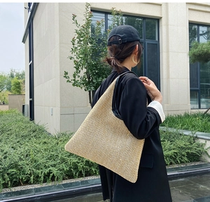 Detail of hand-woven straw tote bag with black leather shoulder straps on a city street