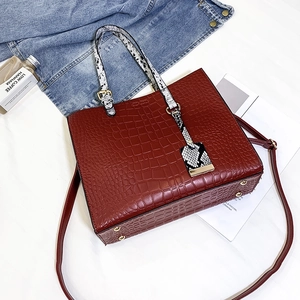 Detail of burgundy crocodile-embossed tote bag with snakeskin pattern handles and studs