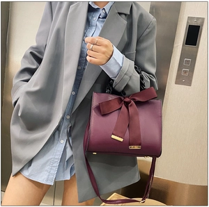 Détail d'un sac à main bordeaux avec un grand nœud décoratif et une chaîne en acrylique