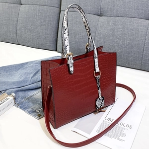 Detail of burgundy crocodile-textured tote bag with snake-skin handles and long strap
