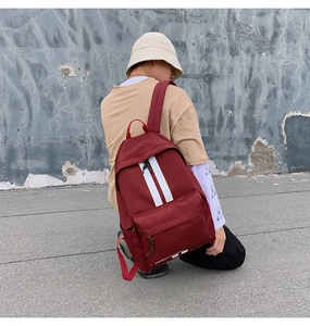 Detail view of burgundy canvas backpack featuring dual white stripes and a front zip pocket