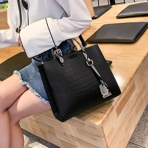 Close-up of black crocodile pattern tote bag with snakeskin print handles and gold hardware