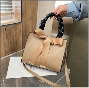 Détail du sac beige en similicuir avec un grand nœud et une poignée tressée noire