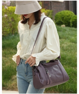 Détail d'un sac bandoulière violet avec surpiqûres en V, franges et pendentif chat