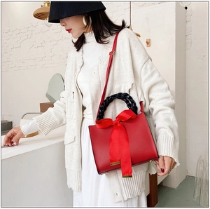 Détail du sac rouge avec poignée anneau tressée noire et grand nœud en ruban satiné