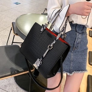 Detail of black faux crocodile handbag with snakeskin pattern handles and red interior