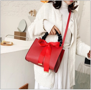 Détail d'un sac à main rouge en cuir avec nœud satiné et poignée tressée sur modèle