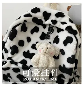 Close-up of white plush bear keychain with pink cheeks on cow print furry backpack