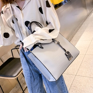 Detail of light gray crocodile texture handbag with contrasting snakeskin pattern handles