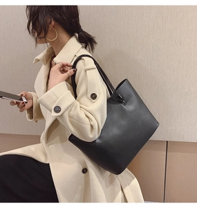 Détail d'un sac cabas en cuir noir porté avec un manteau beige montrant sa grande taille