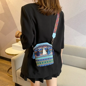 Detail of bohemian straw bucket bag with blue fringe and patterned wide shoulder strap