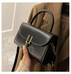 Detail of black matte leather handbag with gold H-shaped clasp and rigid round handle
