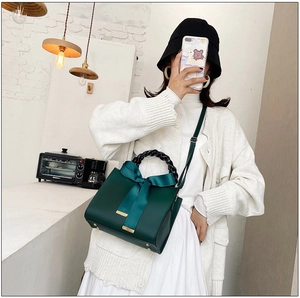 Détail d'un sac à main vert foncé avec nœud en satin, poignée tressée et doré métal