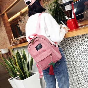 Stylish pink corduroy backpack for women featuring a colorful tassel charm in a cafe setting