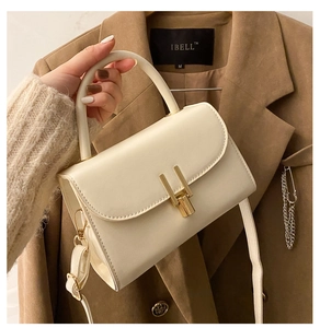 Detail of a white leather crossbody bag with a distinctive gold double-pillar lock
