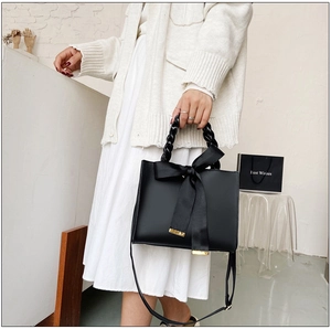 Détail du sac à main noir avec grand nœud en soie et poignée tressée élégante