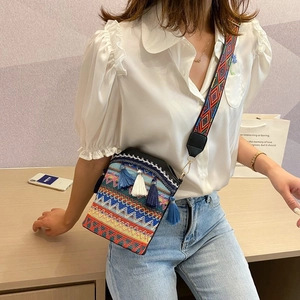 Detail of bohemian straw bucket bag featuring colorful embroidery and tassel charms