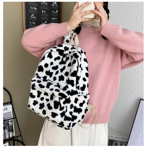 Detail view of the soft cow print plush backpack featuring a secure front zipper pocket