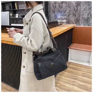 Close-up of a large black canvas travel bag with leather logo held by a model in a cafe