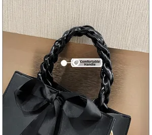 Détail de la poignée tressée et du nœud en ruban noir sur un sac à main en cuir