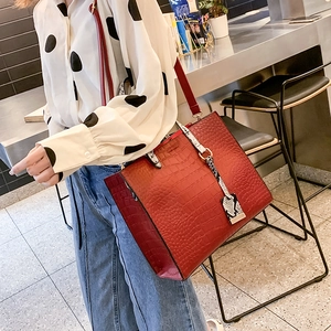 Detail of red croc-embossed tote bag with snakeskin print handles held by a model