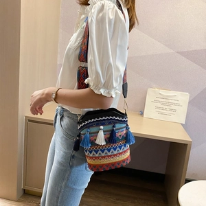 Ethnic woven bucket bag with colorful tassels and geometric strap worn by model