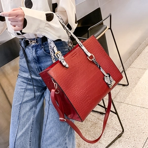 Macro detail of the dark red crocodile embossed tote with contrasting snakeskin straps