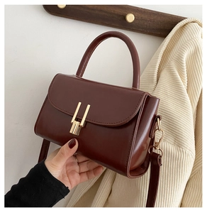 Detail view of burgundy leather small square bag featuring a gold bar lock and top handle