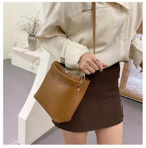 Detail einer braunen Eimertasche mit geprägtem Fashion-Logo und Goldbeschlägen