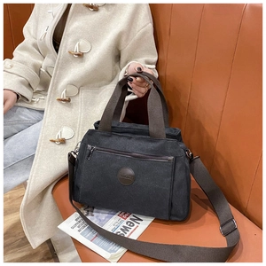 Close-up of a durable black canvas travel bag featuring brown straps on a stylish leather sofa
