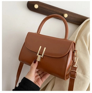 Detail of caramel PU leather handbag with golden H-shaped clasp and hand-held view