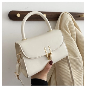 Detailed view of a white structured handbag with a gold H-shaped clasp being held by a model