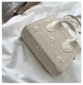 Détail d'un sac cabas en paille avec broderie marguerite et poignées en cuir sur tissu blanc