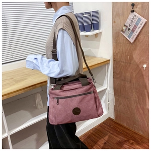 Side view of dusky pink canvas travel bag with brown straps in a cafe setting