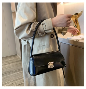 Close-up of a black leather handbag with a gold square clasp on a woman's beige coat
