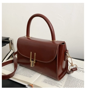 Detail of dark reddish brown square handbag with gold lock and handle on a book