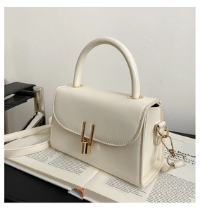 Close-up of cream white leather crossbody bag with gold metal clasp on a magazine