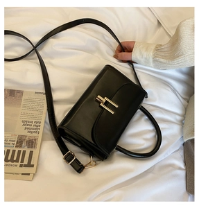 Detail of black leather crossbody bag with golden H clasp and adjustable strap on white sheets