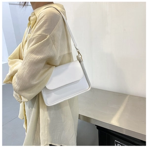 Detailed side view of white faux leather shoulder bag with gold hardware worn by model